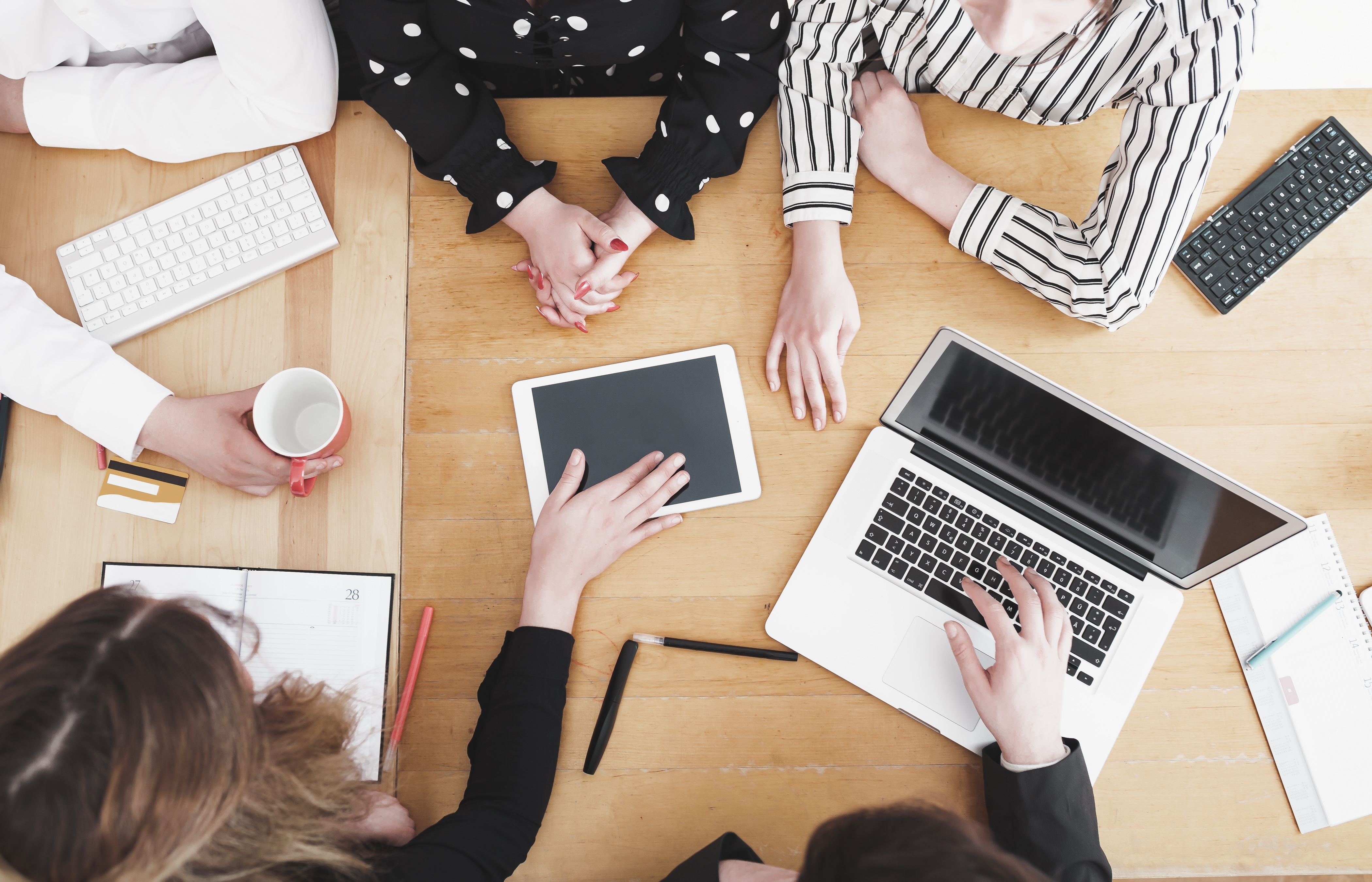 Young business team working together as a group on office desk with multiple electronic devices and paper based tools